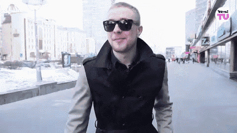 a man wearing sunglasses and a trench coat is walking down a sidewalk