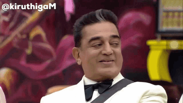 a man in a tuxedo and bow tie is smiling with the words @kiruthigam behind him