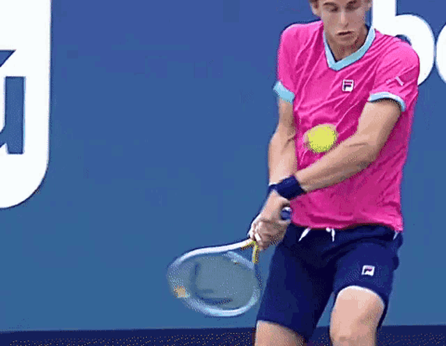 a man in a pink shirt and blue shorts is swinging a tennis racket at a tennis ball