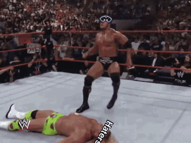 a wrestler is standing over another wrestler in a wrestling ring with a crowd watching .
