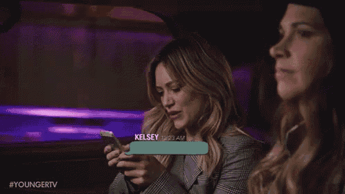two women are sitting in a car and one of them is looking at her phone .