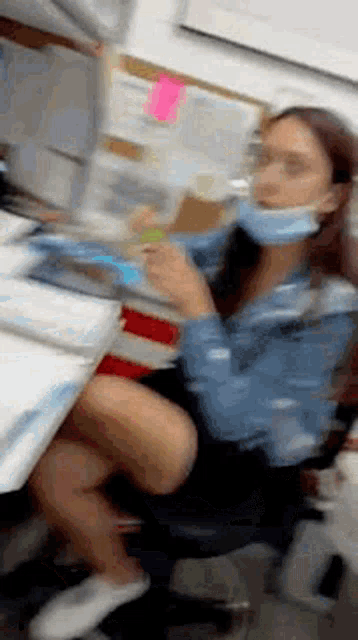 a woman wearing a mask is sitting at a desk with her legs crossed