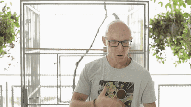 a bald man wearing glasses is standing in front of a bird cage and giving a thumbs up