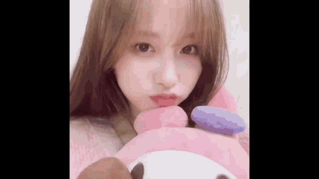 a young woman is holding a pink stuffed animal and making a face .