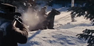 a man in a top hat is holding a gun in the snow while a man on a horse is riding by .