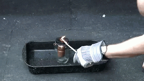 a person wearing gloves is lighting a candle in a jar on a tray