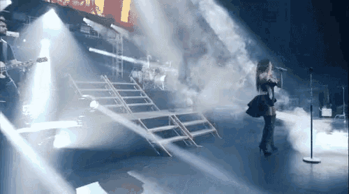 a woman is singing into a microphone on a stage with smoke coming out of it .