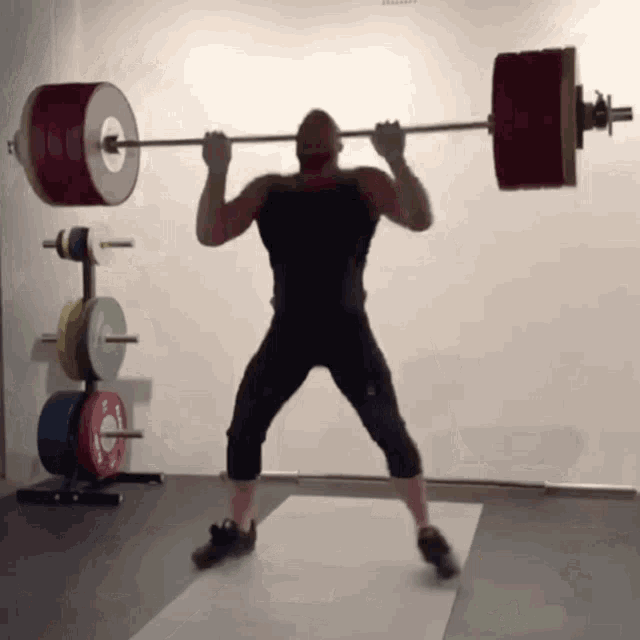 a man is squatting with a barbell over his head and the barbell has a white circle on it