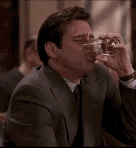 a man in a suit is drinking a glass of water .