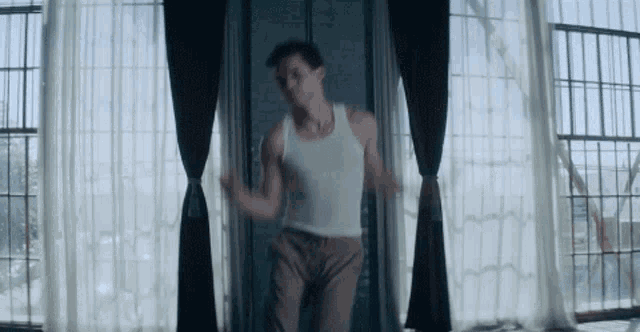 a man in a white tank top is dancing in a room .