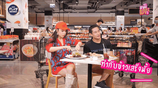 a man and a woman sit at a table in a grocery store with a sign that says play growing
