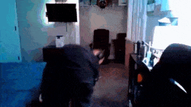 a man is playing a video game in a living room with a tv on the wall .