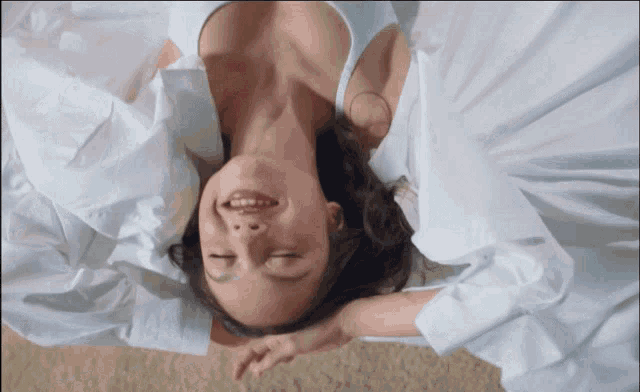 a woman in a white shirt is laying on her back with her eyes closed