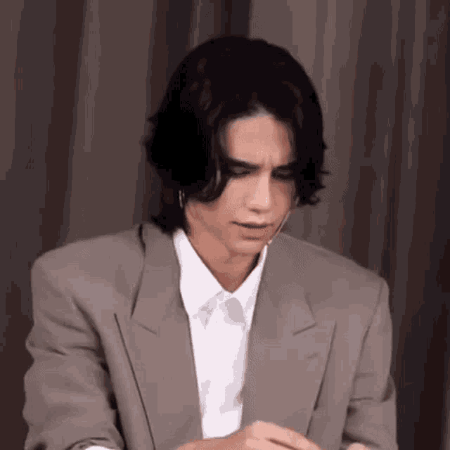 a young man in a suit and white shirt is sitting in front of a microphone .