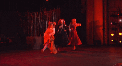 three women are dancing in a dark room with red lights