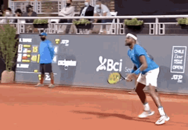 a man in a blue shirt is playing tennis on a court with a bci logo on the wall behind him