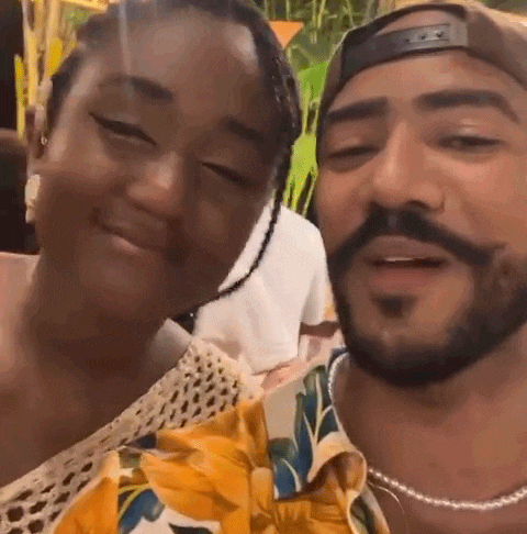 a man and a woman are posing for a picture together . the man has a beard and the woman has braids .