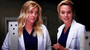 two women in lab coats are standing next to each other and smiling .