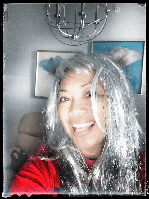 a woman wearing a silver wig is smiling in front of a chandelier