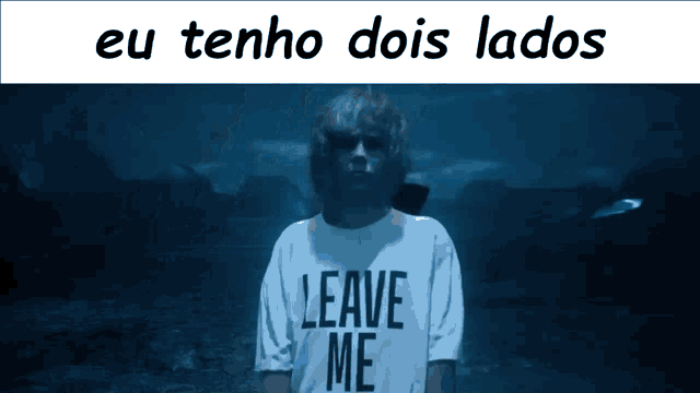 a man wearing a leave me shirt stands in the dark