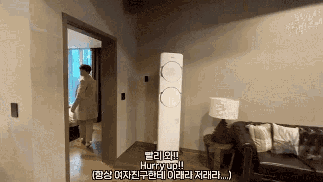 a man is walking into a living room with a couch and a lamp and says hurry up