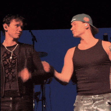 two men shaking hands on a stage with one wearing a hat