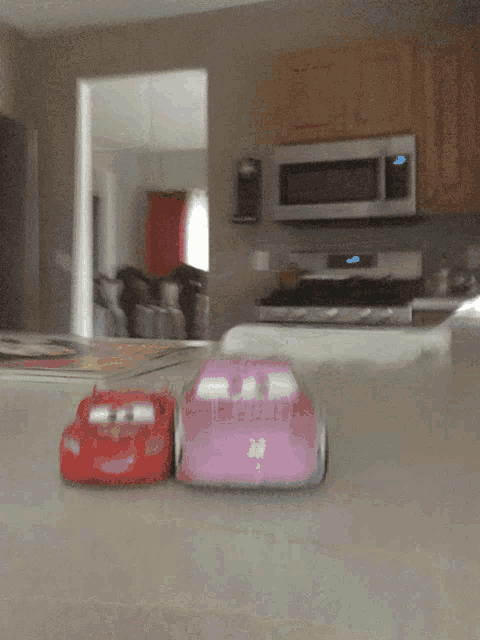a red toy car and a pink toy car are sitting on a counter