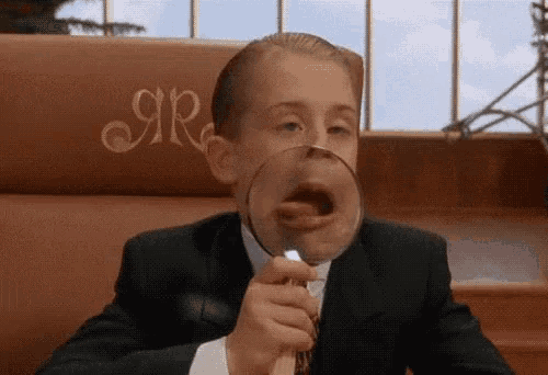 a young man in a suit is holding a magnifying glass in front of his face .