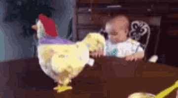 a baby is sitting at a table with a stuffed chicken and a toy chicken .
