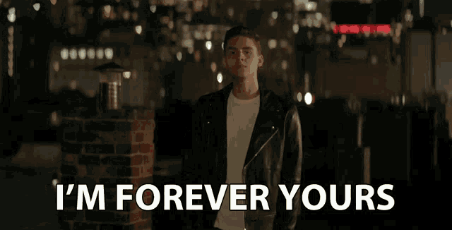 a man in a leather jacket is standing in front of a sign that says i 'm forever yours
