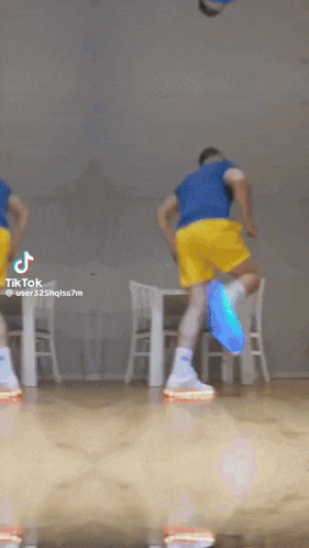 a man in a blue shirt and yellow shorts is dancing in front of a table and chairs .