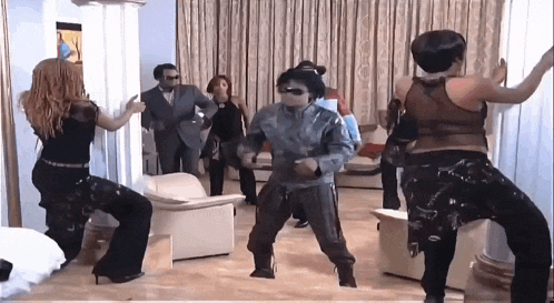 a group of people are dancing in a living room with a man wearing sunglasses .
