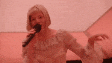 a woman is singing into a microphone while standing in front of a pink wall .