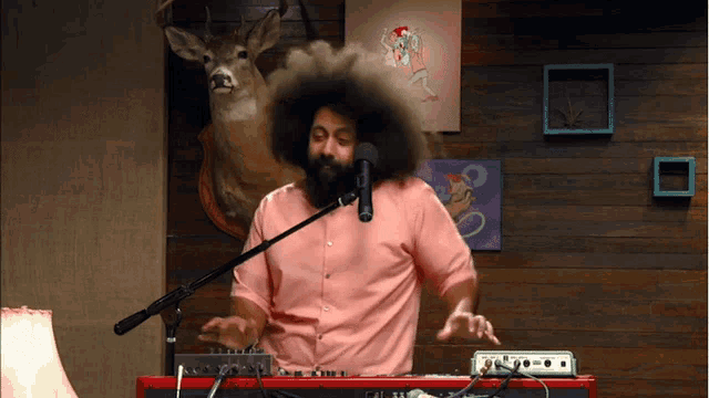 a man in a pink shirt is singing into a microphone while playing a keyboard