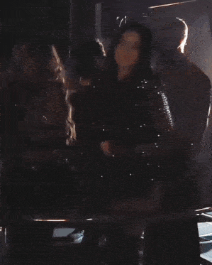 a group of people standing in a dark room with a man in a red jacket