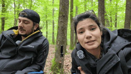 a man and a woman are sitting in the woods and the man is wearing a jacket that says columbia