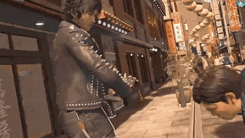 a man in a leather jacket is standing next to another man on a sidewalk in a video game .