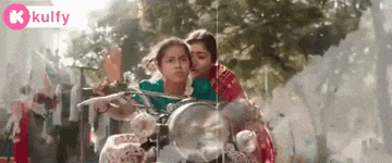 two women are riding a motorcycle on a street and one of them is kissing the other .