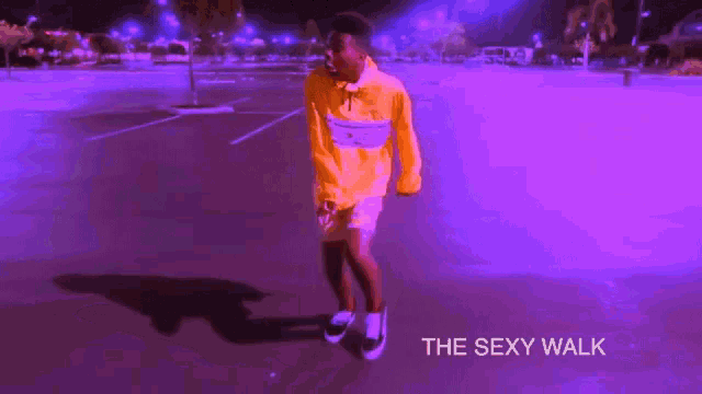 a man in a yellow hoodie is dancing in a parking lot with the words " the sexy walk " below him