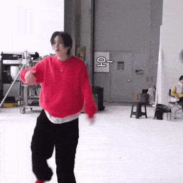 a young man in a red sweater and black pants is dancing in a room .