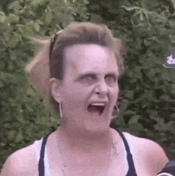 a woman is making a funny face with her mouth open in front of a bush .