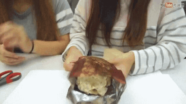 a woman is holding a piece of food wrapped in tin foil while another woman looks on .