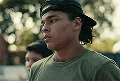 a young man wearing a hat and a green shirt looks to the side