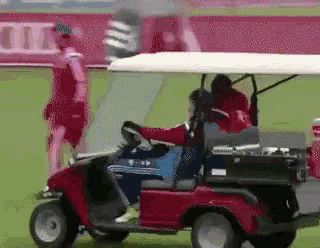 a man in a red shirt is driving a golf cart on a soccer field