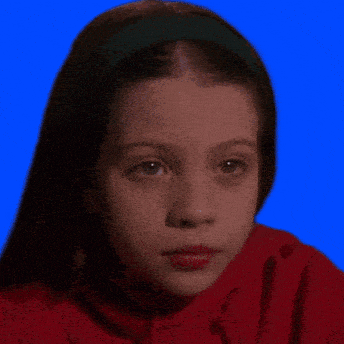a young girl wearing a red shirt and a green headband is looking at the camera .