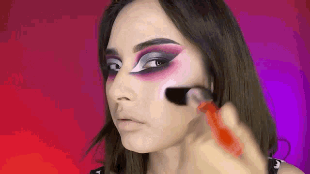 a woman is applying makeup to her face using a brush .