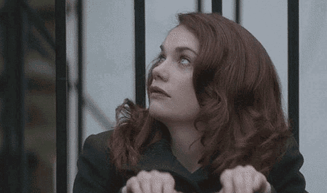 a woman with red hair is standing in front of a fence looking up .