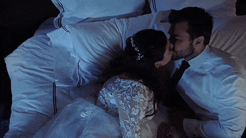 a bride and groom are kissing on a bed
