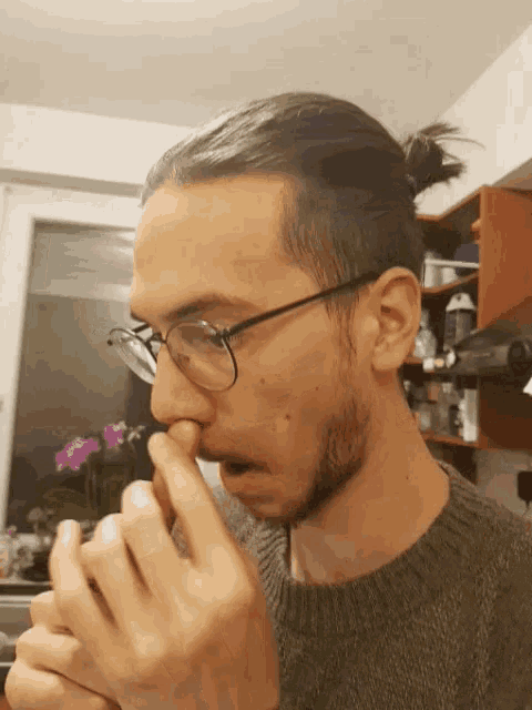 a man wearing glasses and a ponytail is holding his nose
