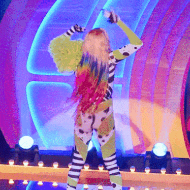 a woman with rainbow hair is dancing on a stage with lights